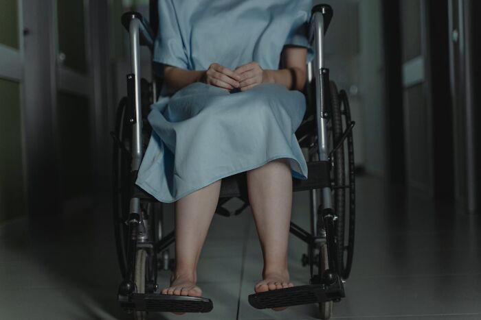 Person in a wheelchair wearing a hospital gown sitting in a dimly lit medical hallway representing medical facts.