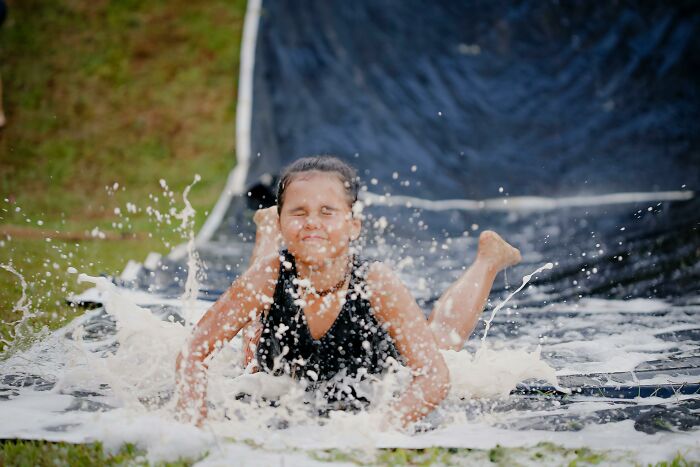 Child sliding down a soapy water slide outdoors, illustrating kids' dumb childhood moments and lack of survival instincts.