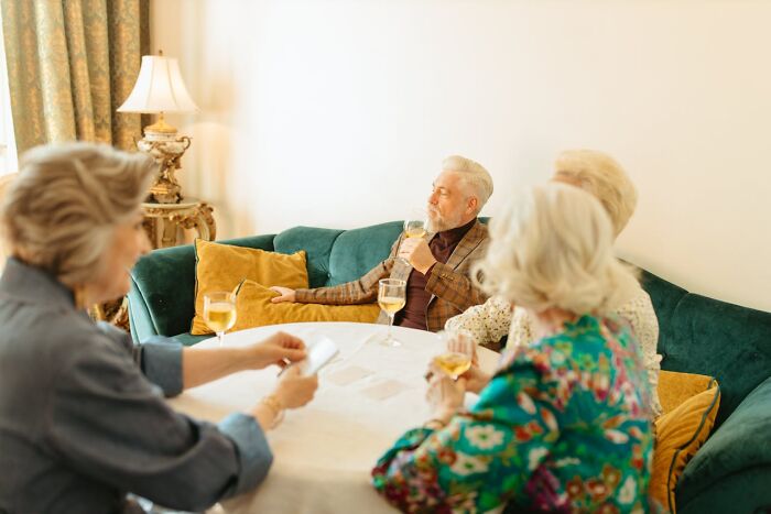 Group of elderly people sitting around a table enjoying drinks in a cozy room, creating a comforting atmosphere.