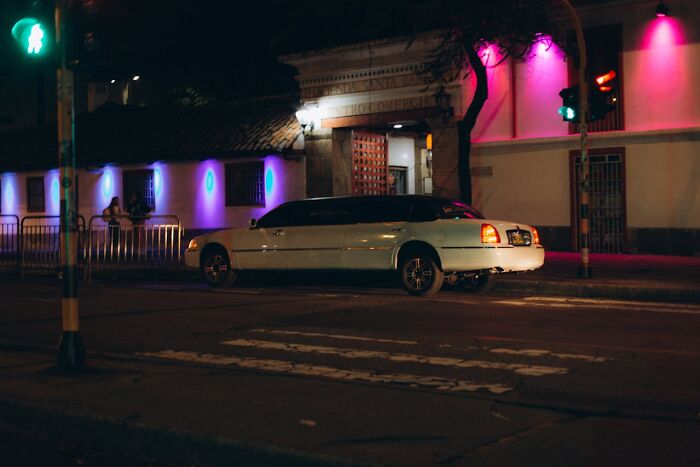 White stretch limousine parked on a city street at night with colorful lights, hinting at wild bachelor party scenes.
