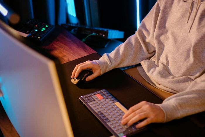 Person wearing a hoodie using a keyboard and mouse at a computer desk, illustrating betrayal and shock online.