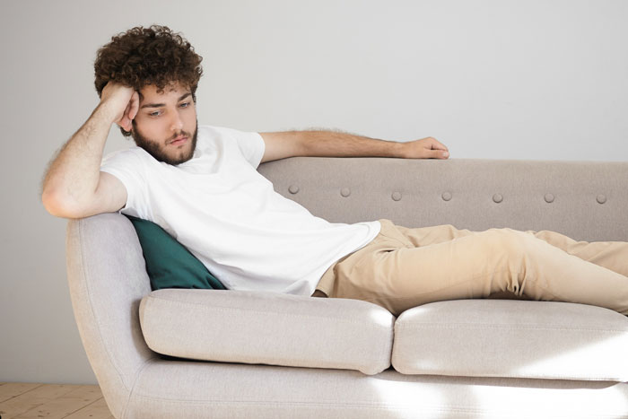 Young man looking distressed while lying on a couch, representing conflict around pregnant girlfriend and pregnancy issues.