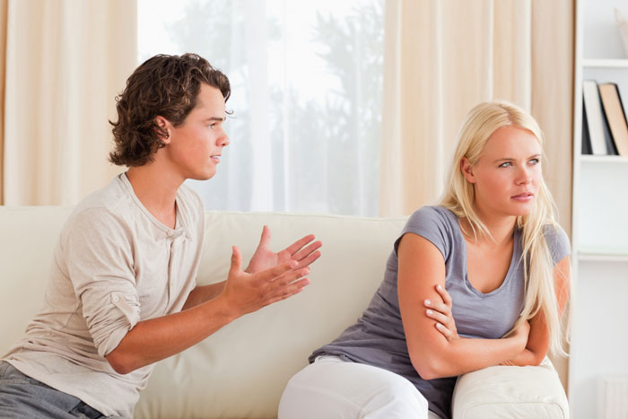 Pregnant girlfriend and boyfriend having a tense argument on the couch about pregnancy and relationship issues.