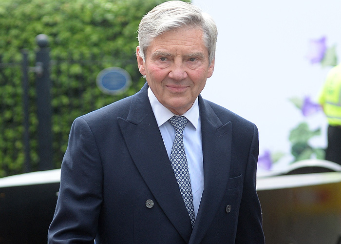 An older man in a navy suit and patterned tie, smiling subtly. Could be a Prince Louis family comparison.