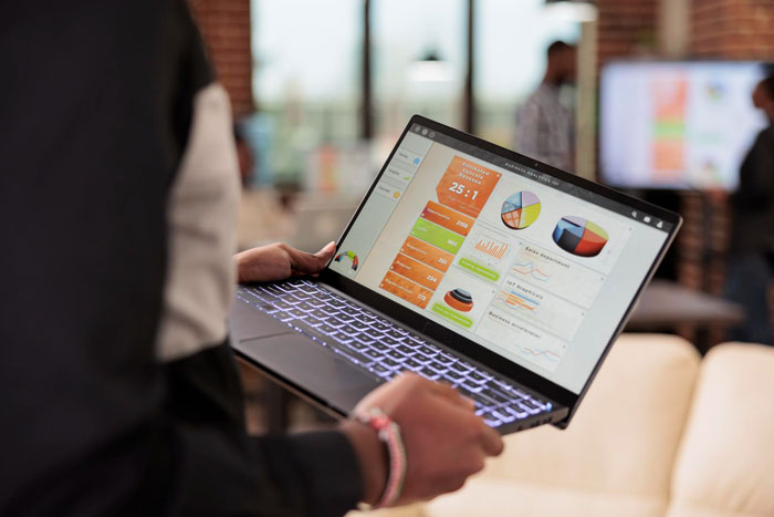 Person holding a laptop displaying colorful charts and graphs, illustrating project sabotage in a work environment.