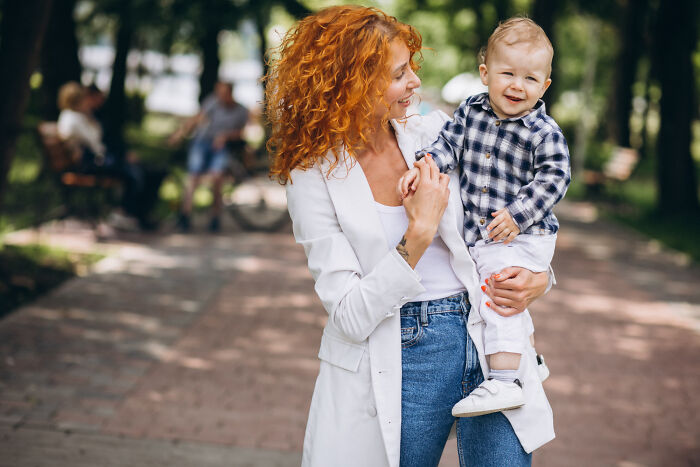 Woman with curly red hair holding a toddler outdoors, capturing a moment full of unexplained psychic session stories.