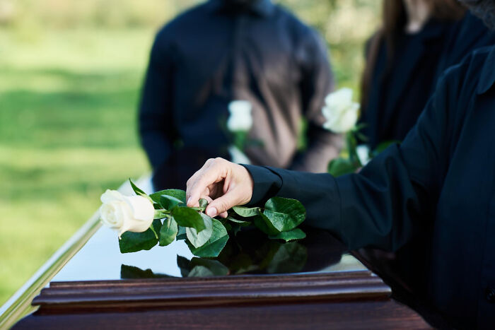 Person placing white rose on coffin during a somber moment in a psychic session with unexpected stories revealed.