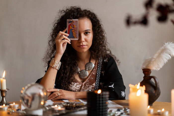 Woman holding a tarot card during a psychic session surrounded by candles and mystical objects, sharing unexplained stories.