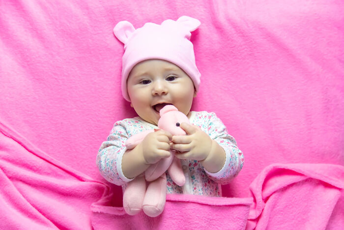 Baby in a pink hat and pajamas holding a soft toy on a pink blanket, unrelated to psychic session stories.