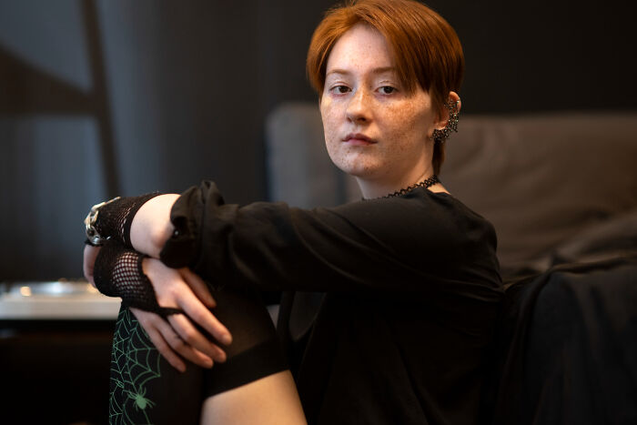 Red-haired person in black clothing sitting indoors, capturing the mysterious vibe of a psychic session story.