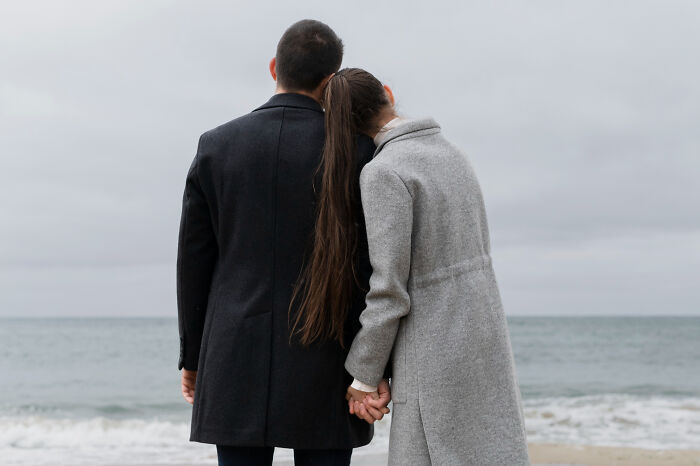 Couple holding hands on a beach, looking at the sea, evoking mysterious psychic session stories.