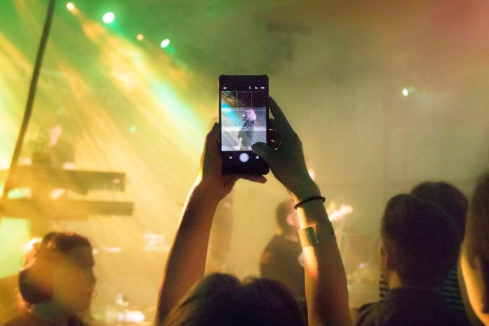 Woman using comedy to cope with ex-BF&rsquo;s trauma, captured on phone amid dimly lit concert crowd.