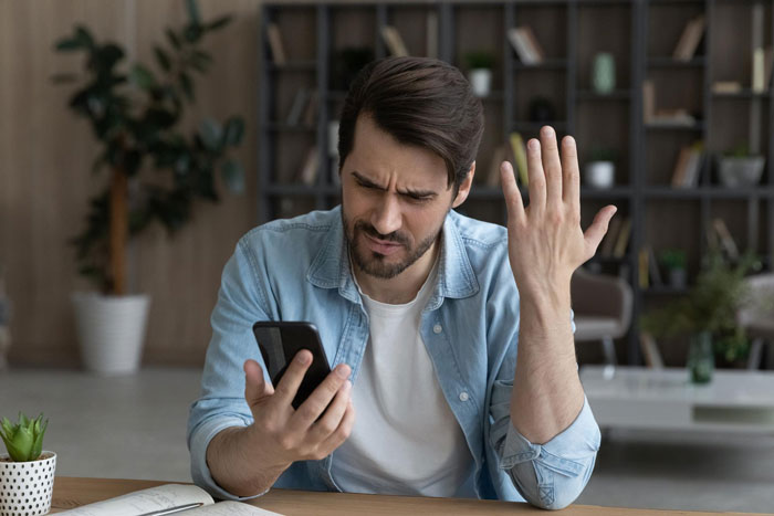 Man with frustrated expression looking at phone, illustrating tension related to stalking and trauma coping issues.