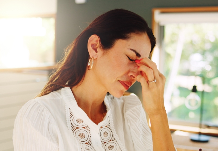 A woman in a white blouse pinching her nose, looking stressed. This image evokes the feeling of entitlement at a wedding table.