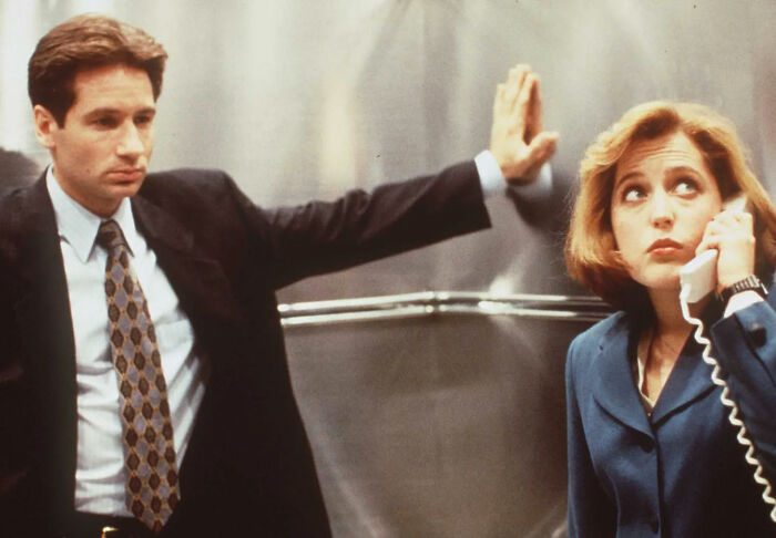 Estrela de TV dos anos 90 parecendo irreconhecível usando saia e peruca loira durante as filmagens, com um novo visual ousado