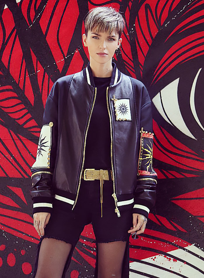 Person wearing a black leather jacket with patches standing in front of a red and black artistic wall mural. Person wearing a black leather jacket with patches standing in front of a red and black artistic wall mural.