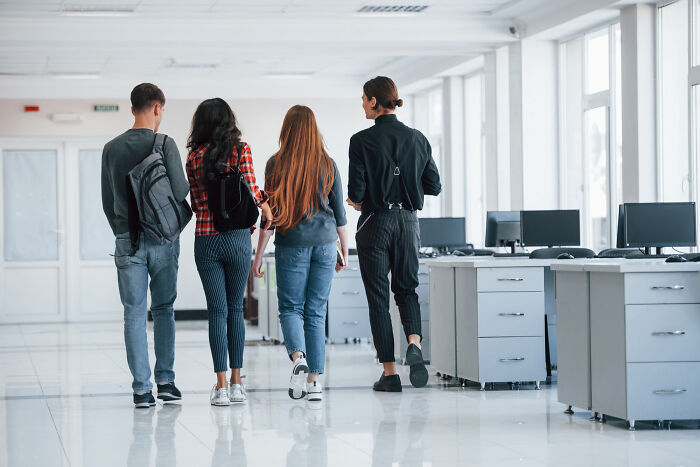 Students walk through a modern office, symbolizing absurd rules in schools and workplaces.
