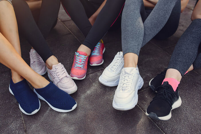 Several pairs of feet in athletic shoes and leggings, sitting on dark ground. Absurd rules.