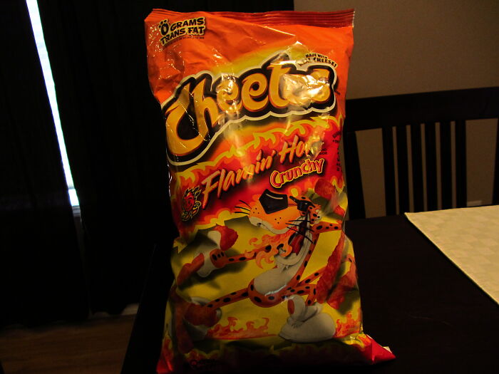 A large bag of Cheetos Flamin Hot Crunchy chips on a dark table. An example of absurd rules implemented by schools.