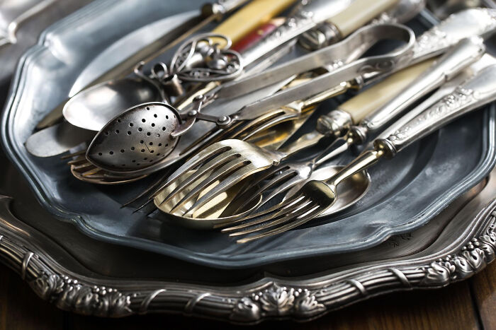 A pile of antique silver utensils on ornate trays. Many absurd rules surround old traditions.