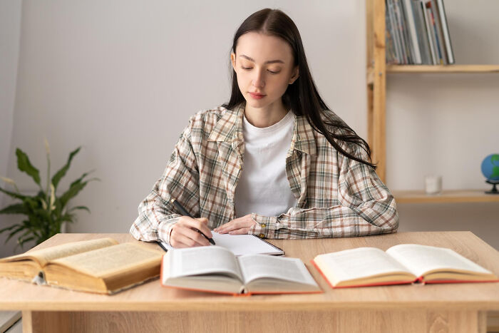 Young woman in a plaid shirt studying with books, illustrating schools and workplaces challenges.