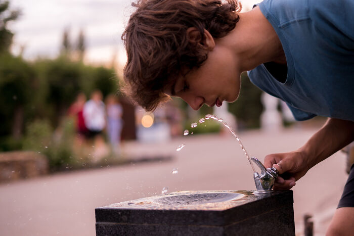 A young person drinks from a water fountain, with water splashing. Absurd rules sometimes fail at schools and workplaces.
