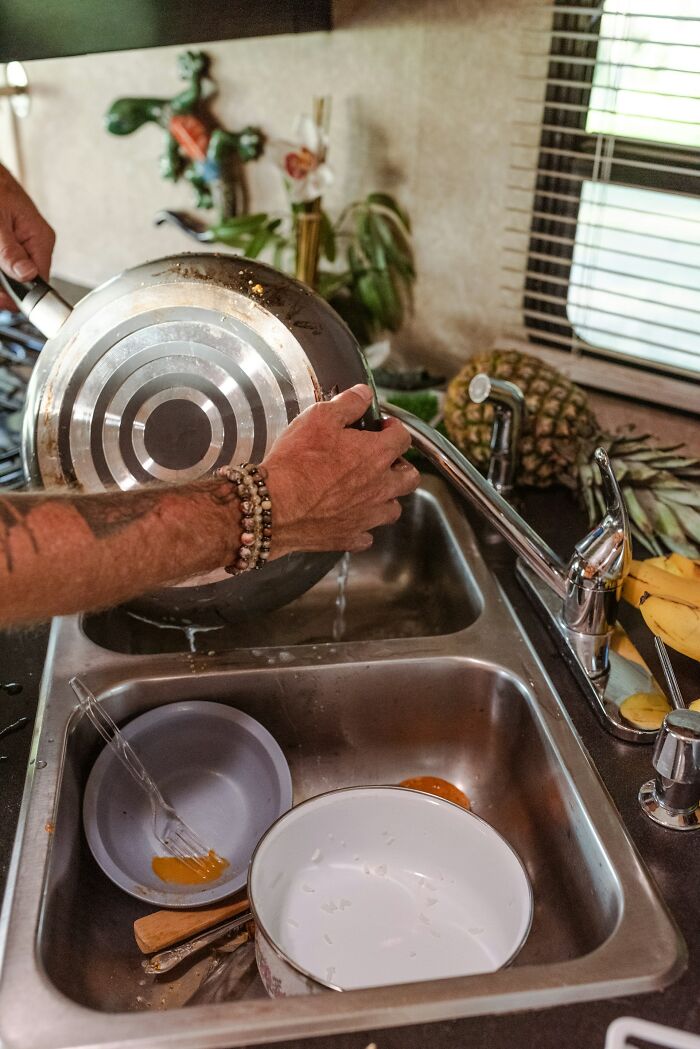 Person washing dirty dishes in kitchen sink, illustrating weaponized incompetence in daily chores.