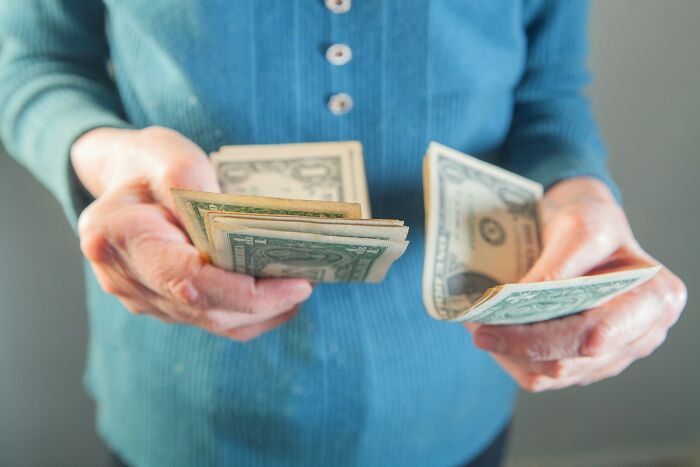 Hands of a person in a blue shirt counting US dollar bills. This relates to stories about a MIL.