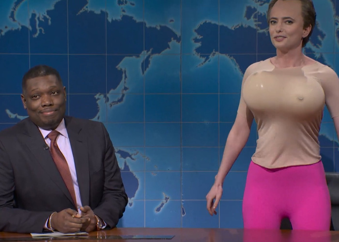 SNL comedian and anchor in front of a world map background during a sketch mocking Bryan Noem amid scandal.