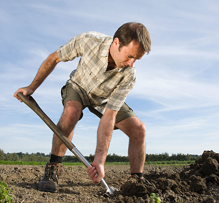 A man in a plaid shirt and shorts digging with a shovel in a field, evoking scary experiences and things to forget.