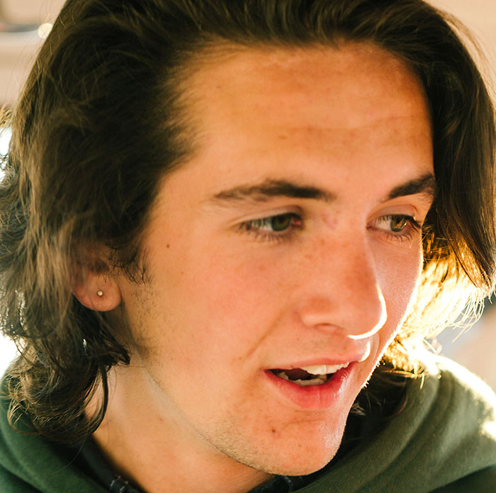 Close-up of a young man with long brown hair, looking right with mouth slightly open, reflecting on scary experiences.