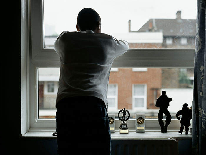 Silhouetted person looking out a window with trophies on the sill. It suggests scary experiences and things people wish to forget.