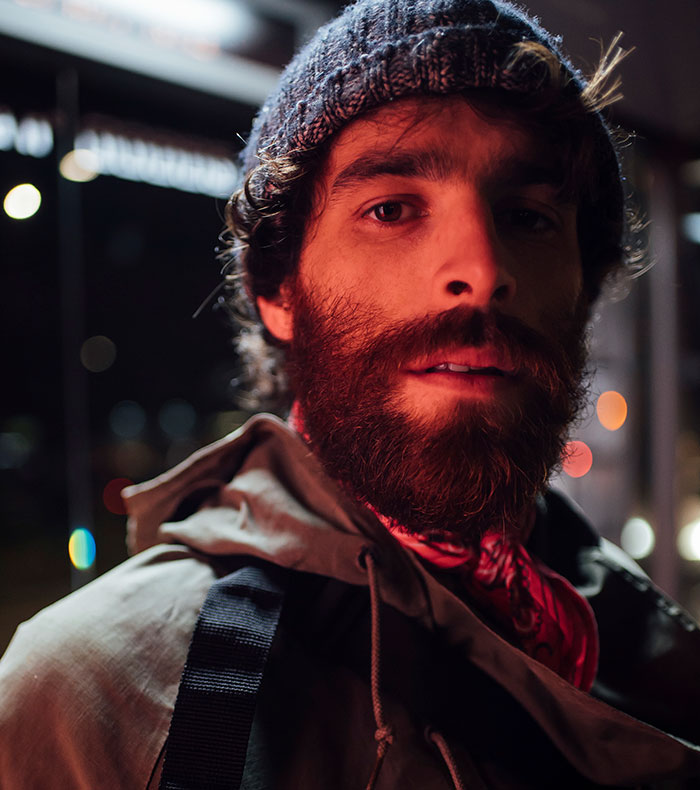 Man with red-tinted beard and knit hat, looking directly at the camera at night, perhaps after a scary experience.