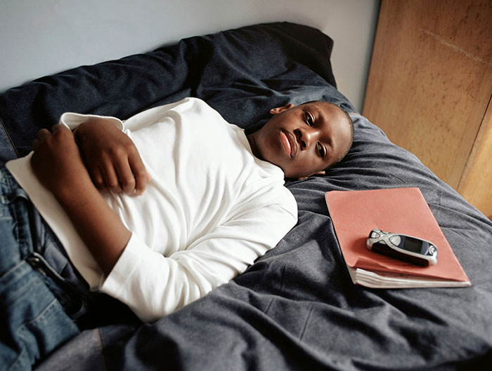 Young man lying on a bed with a book and old phone nearby, contemplating scary experiences people wish to forget.