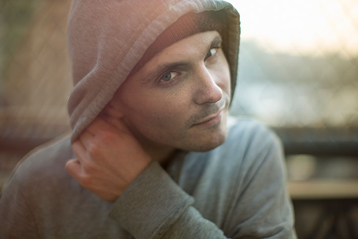 A man in a grey hoodie looks over his shoulder, a hand near his neck. He embodies the feeling of scary experiences.