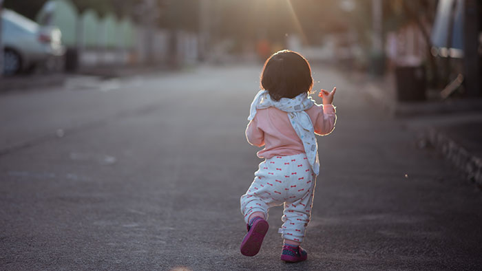 A toddler walks away on an empty street as the sun sets. This image evokes feelings from scary experiences.