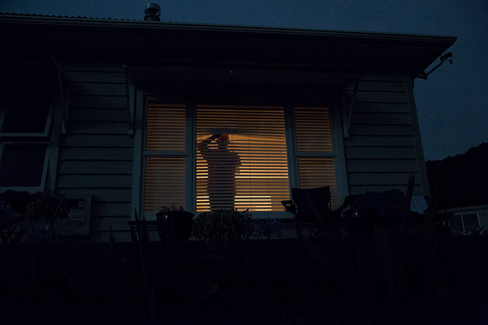 Silhouette of a person looking out a window through blinds at night, evoking scary experiences.