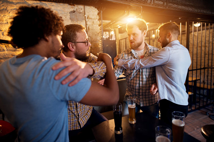 Four men arguing intensely in a dimly lit bar, highlighting conflict and tension related to unstable relationships.
