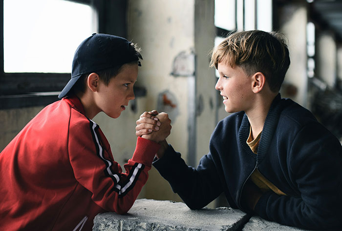 Two kids in school arm wrestling, showing determination and competitiveness in a playful moment among peers.
