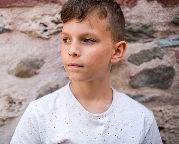 Young boy standing against a stone wall, reflecting on moments that earned him the weirdo title in school.