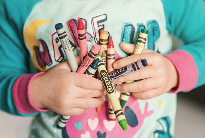 Child holding colorful crayons in hands, illustrating kids in school who earned the weirdo title stories.