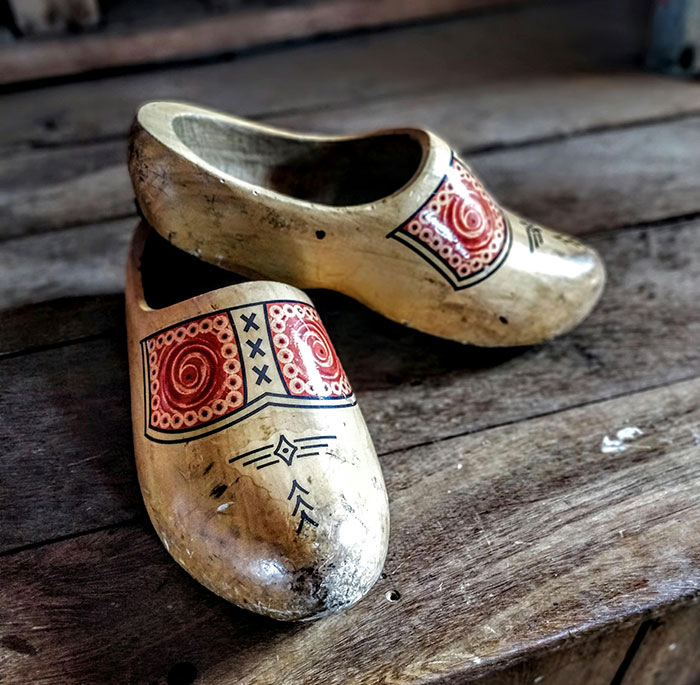 Pair of vintage wooden clogs with red and black designs sitting on a rustic wooden floor in a school setting.
