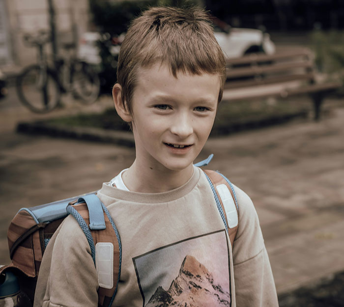 Young boy with a backpack smiling outdoors, representing kids in school who earned the weirdo title stories.