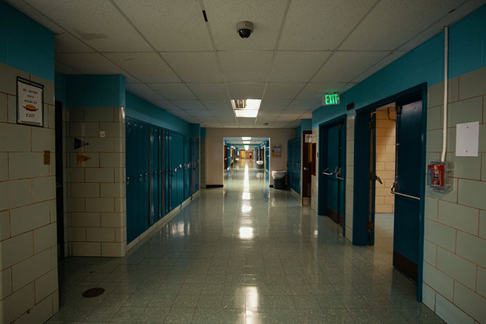 Empty school hallway with blue lockers and open classroom doors, representing kids in school who earned weirdo title.