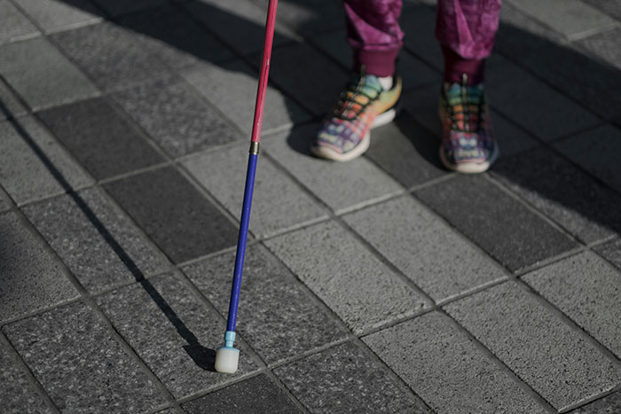 Child wearing colorful shoes and purple pants using a cane while walking on a tiled school pavement outdoors.