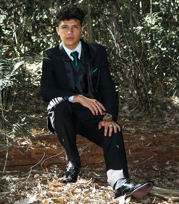 Teen boy dressed formally sitting outdoors in a wooded area, representing kids in school who earned the weirdo title.