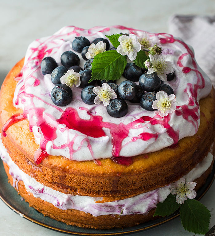 Blueberry cake with cream frosting and berry drizzle, styled with flowers, representing kids in school labeled weirdo.