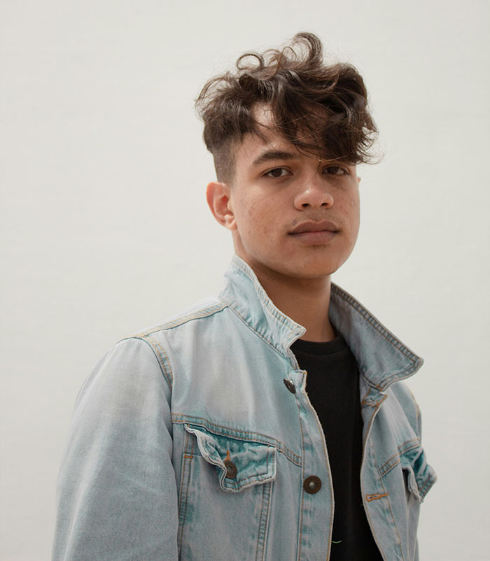 Teen boy with curly hair wearing a denim jacket looking confidently representing kids in school labeled weirdo.