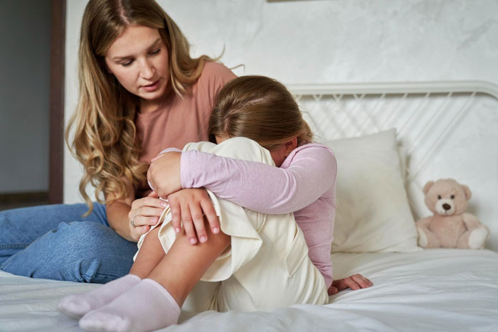 Mother comforting daughter sitting on bed, daughter showing fear and anxiety, school suspending daughter fear snakes issue. Mother comforting daughter sitting on bed, daughter showing fear and anxiety, school suspending daughter fear snakes issue.