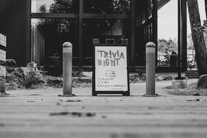 Black and white photo of a sidewalk sign advertising trivia night, inviting people to test their general knowledge skills. Black and white photo of a sidewalk sign advertising trivia night, inviting people to test their general knowledge skills.